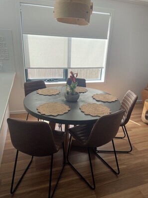 Een eetruimte met een ronde tafel, vier stoelen, een vaas met bloemen en een hanglamp.