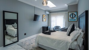 Un dormitorio moderno con una cama grande, un televisor de pantalla plana, una silla y obras de arte en las paredes.