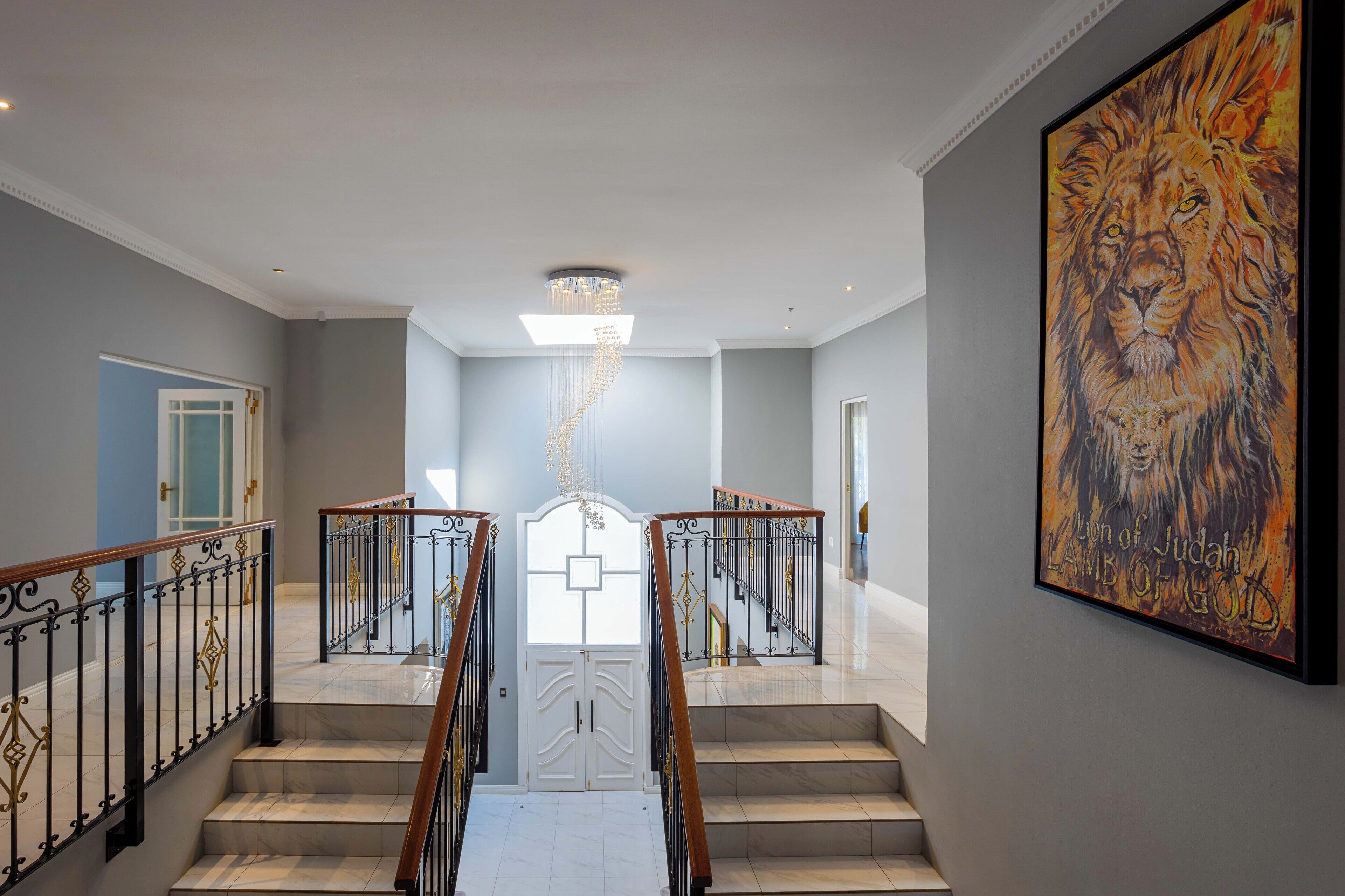 Uma imponente escadaria com um candelabro, um quadro de um leão e uma porta que dá para outro cômodo.