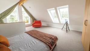 Een slaapkamer met een schuine kap, een bed, een rode stoel en een statief in de hoek.
