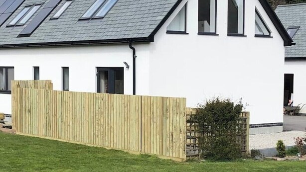 Een modern herenhuis met twee verdiepingen, een schuin dak, dakramen en een houten omheining.