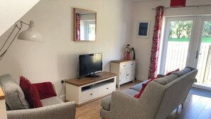 Een woonkamer met een televisie op een houten dressoir, grijze banken, een klein wit kastje en een spiegel met rode lijst.