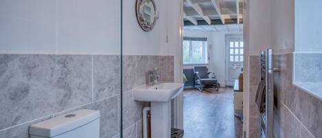 A bathroom with a toilet, sink, and shower. There is a glass partition, a towel rack, and a radiator.