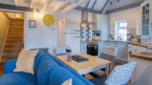Una cocina acogedora con zona de comedor, que incluye una escalera de madera, un sofá azul y una mesa con un hervidor y un libro.