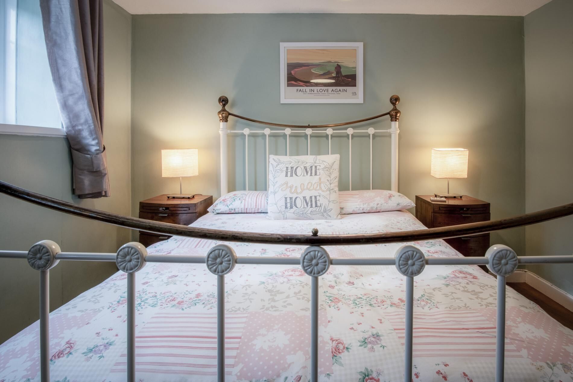 Een slaapkamer met een hemelbed, bloemenbeddengoed, twee nachtkastjes met lampen, een ingelijst schilderij aan de muur en een raam met gordijnen.