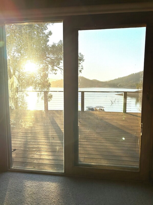 A view from a room with a large window overlooking a wooden deck and a body of water.