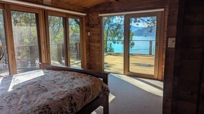 A bedroom with a bed, large windows, and a view of a lake.