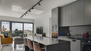 A modern kitchen with a central island, built-in appliances, and a large window offering a city view. - Phaedrus Living: Paphos Noir Residence (Paphos)