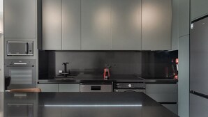 A modern kitchen with grey cabinetry, a black countertop, a built-in microwave, a coffee machine, and a refrigerator. - Phaedrus Living: Paphos Noir Residence (Paphos)