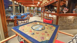 A cozy, well-lit room with wooden furniture, a large table with seashells, and a bar area with bottles and glasses.