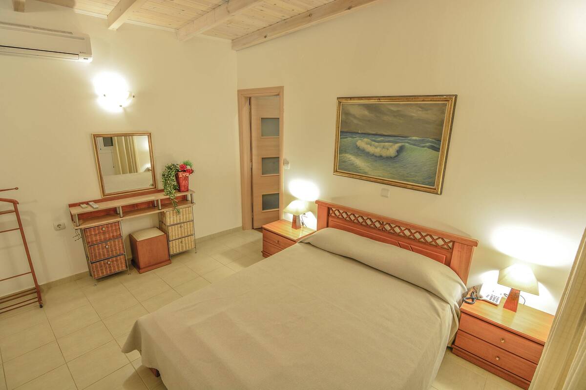 Een slaapkamer met een bed, nachtkastjes, een kaptafel, een spiegel, een schilderij en een airconditioning.
