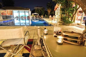 An outdoor swimming pool area at night with lounge chairs and a bar area. - Green Village (Xylokastro-Evrostina)