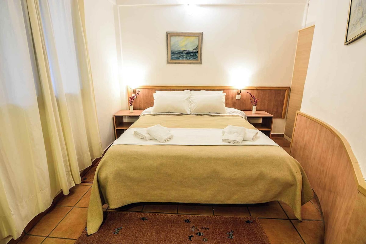 Een hotelkamer met een bed, twee nachtkastjes, een schilderij aan de muur en een bruin vloerkleed.