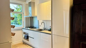 A compact kitchen with white cabinets, a gas stove, a sink, and a window overlooking greenery.