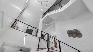 Un intérieur à plusieurs niveaux, avec un escalier, des murs blancs et un luminaire au plafond.
