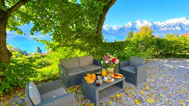 An outdoor seating area with a table set for breakfast, surrounded by greenery and a scenic mountain view.