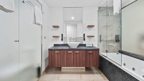 A modern bathroom with a glass shower enclosure, a white sink, and wooden cabinets.