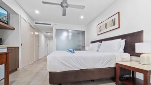 A hotel room with a bed, bedside table, ceiling fan, and a TV on a shelf.
