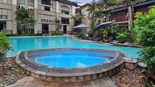 A hotel with a swimming pool surrounded by lush greenery and palm trees.