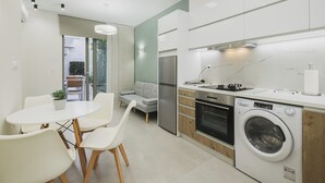 Eine moderne Küche mit integriertem Waschmaschinenanschluss, ein Essbereich mit Tisch und Stühlen sowie ein graues Sofa.