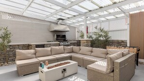 Eine Terrasse im Freien mit einer Steinwand, einem großen beigefarbenen Ecksofa, einem Couchtisch und einem Kicker.