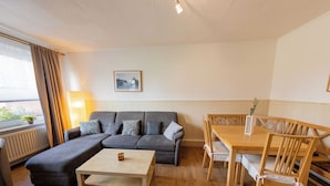 A modern living room with a grey sectional sofa, a wooden coffee table, and a dining table with chairs. - "Windstille" - your retreat at the Deichkieker guesthouse - pets allowed (Wangerland)
