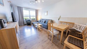A modern, well-lit room with a wooden dining table, a sofa, and a TV on a stand. - "Windstille" - your retreat at the Deichkieker guesthouse - pets allowed (Wangerland)