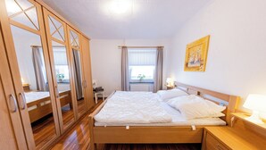 A bedroom with a wooden bed, a nightstand, a wardrobe, and a window with curtains. - "Windstille" - your retreat at the Deichkieker guesthouse - pets allowed (Wangerland)