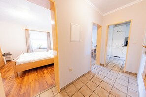 A bedroom with a wooden bed, a window with curtains, and a view into the kitchen. - "Windstille" - your retreat at the Deichkieker guesthouse - pets allowed (Wangerland)