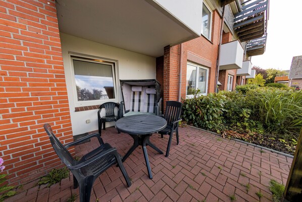 Eine Terrasse mit einem runden Tisch und vier Stühlen, eine Ziegelwand und ein Fenster mit Jalousien.