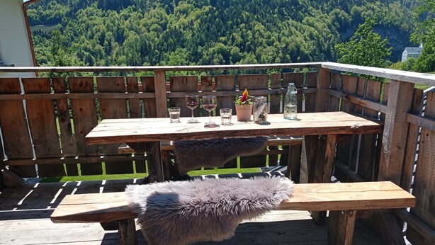 A wooden deck with a table and bench, surrounded by a wooden fence, overlooking a forested hillside. - Apartment in Stans near Wolfsklamm River (Stans)