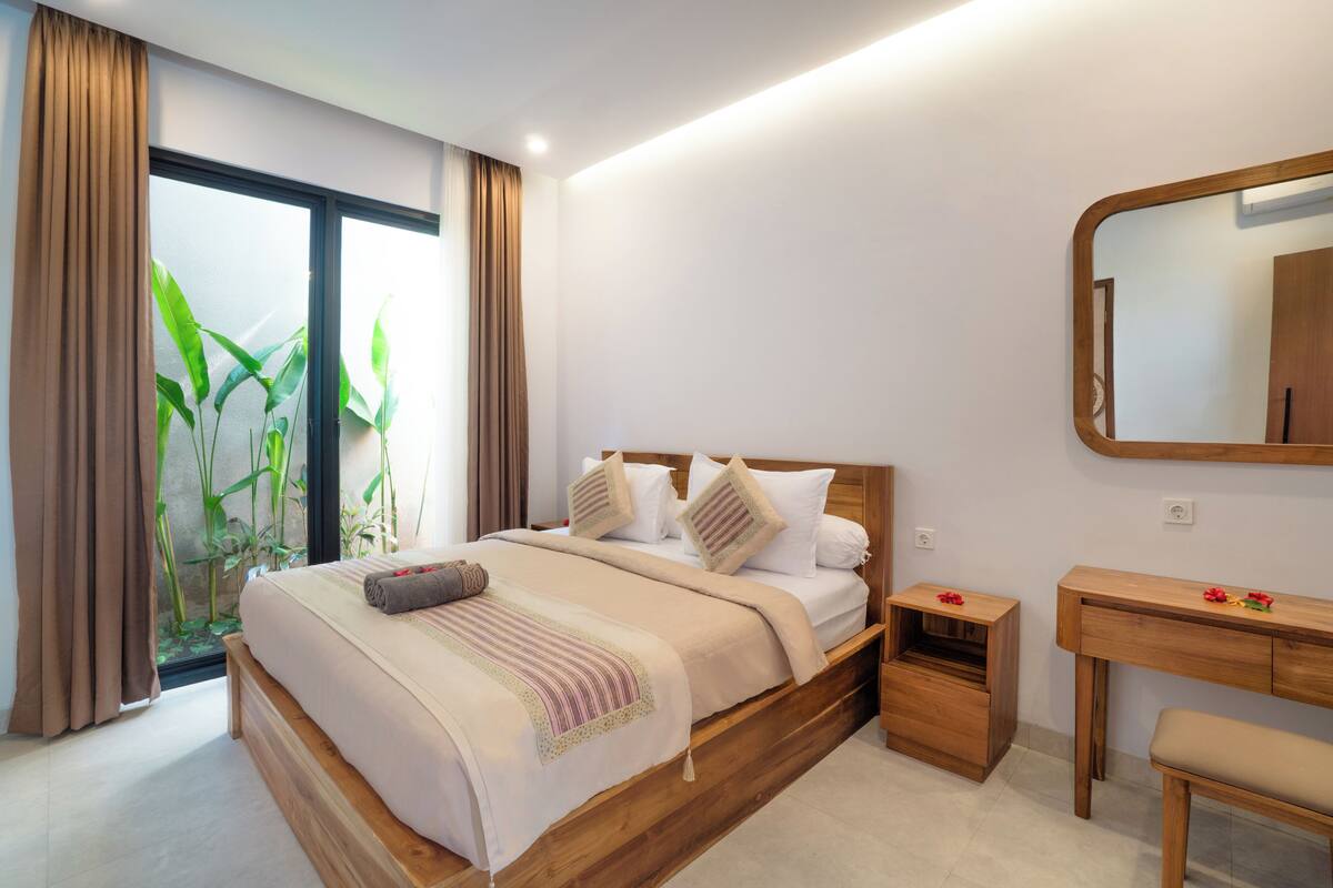 Une chambre à coucher moderne avec un lit en bois, une petite table de chevet, une commode en bois et un grand miroir.