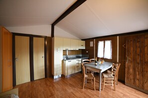A compact kitchen with wooden cabinets, a dining table with chairs, and a window with curtains.