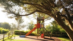 A playground with a slide and climbing structure surrounded by trees.