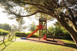Un parque infantil con un tobogán y estructura para escalar, rodeado de árboles.