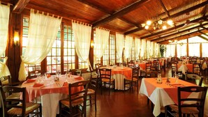 A large dining hall with multiple tables, wooden beams, and large windows with curtains.