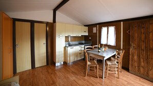 Een compacte keuken met houten kastjes, een eettafel met stoelen en een raam met gordijnen.