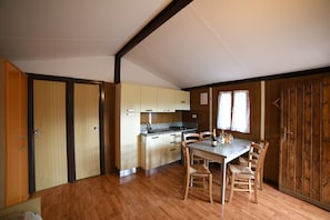 A compact kitchen with wooden cabinets, a dining table with chairs, and a window with curtains.