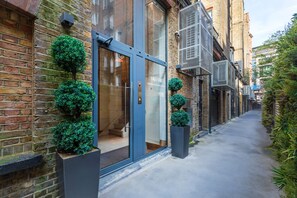 Une ruelle étroite bordée d’un bâtiment moderne doté de grandes portes vitrées, de murs en briques et de plantes ornementales en pot.
