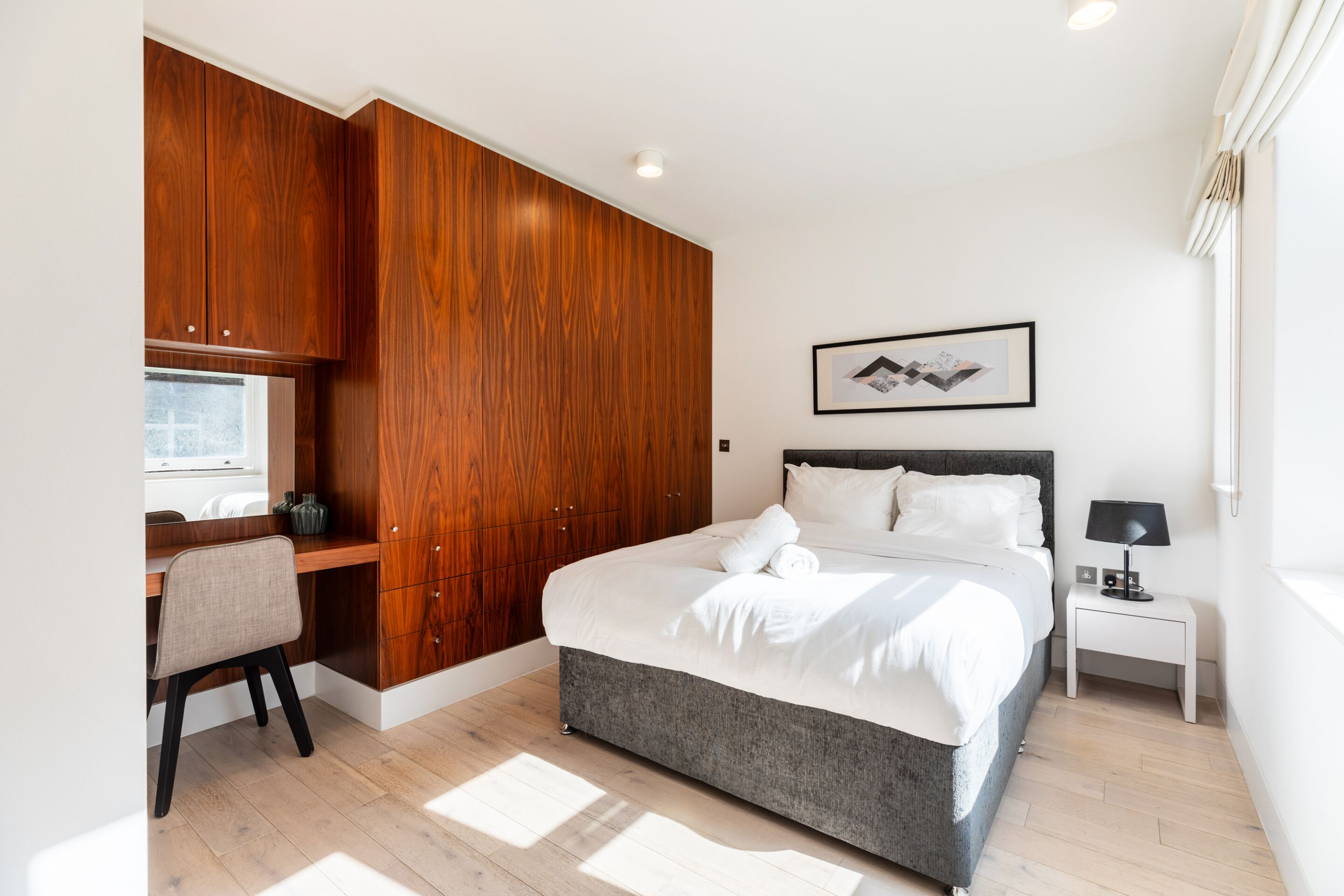 A modern bedroom with a large bed, a desk, and a wardrobe.