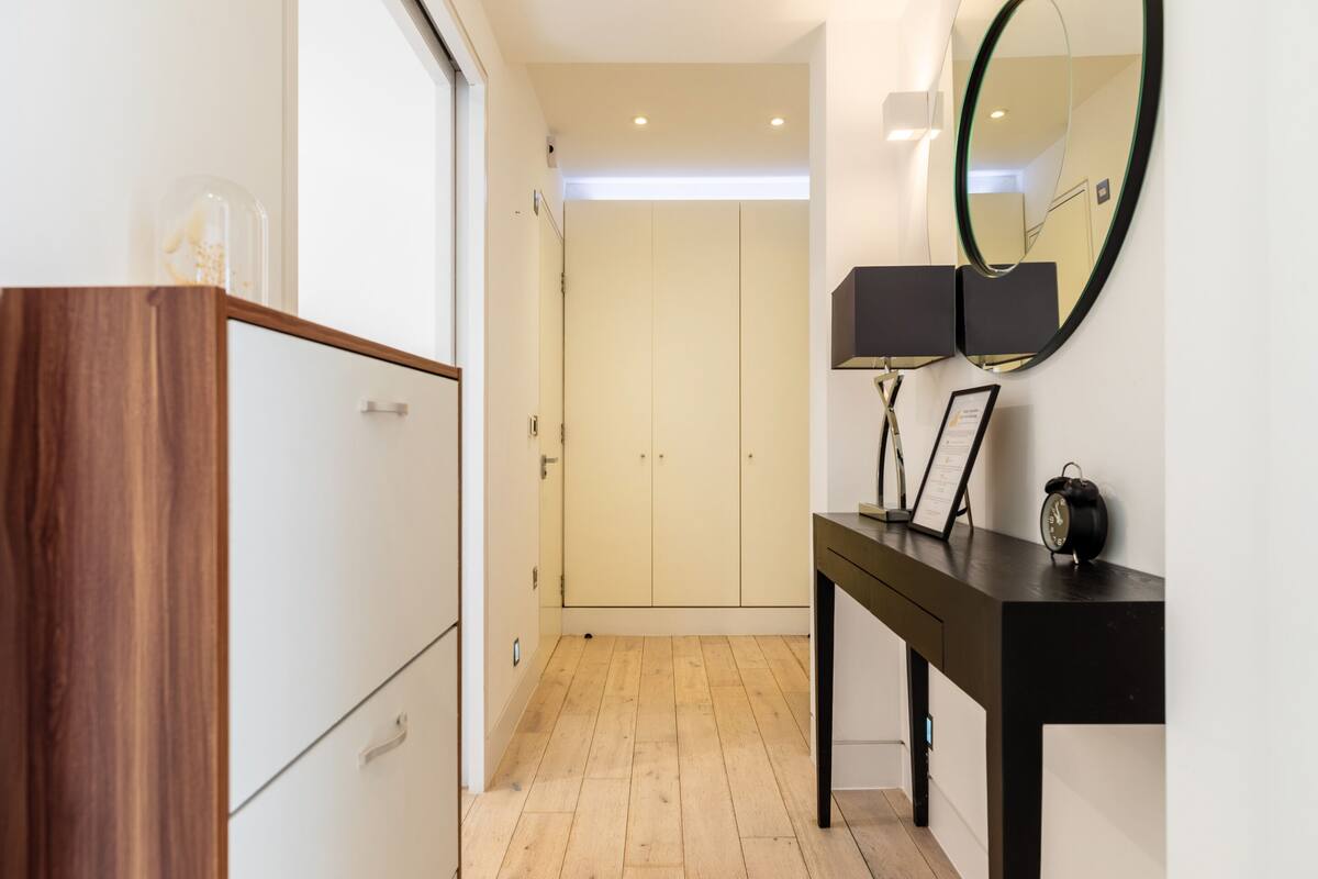 A hallway with a wooden wardrobe, a black desk with a mirror, and a door leading to a room.