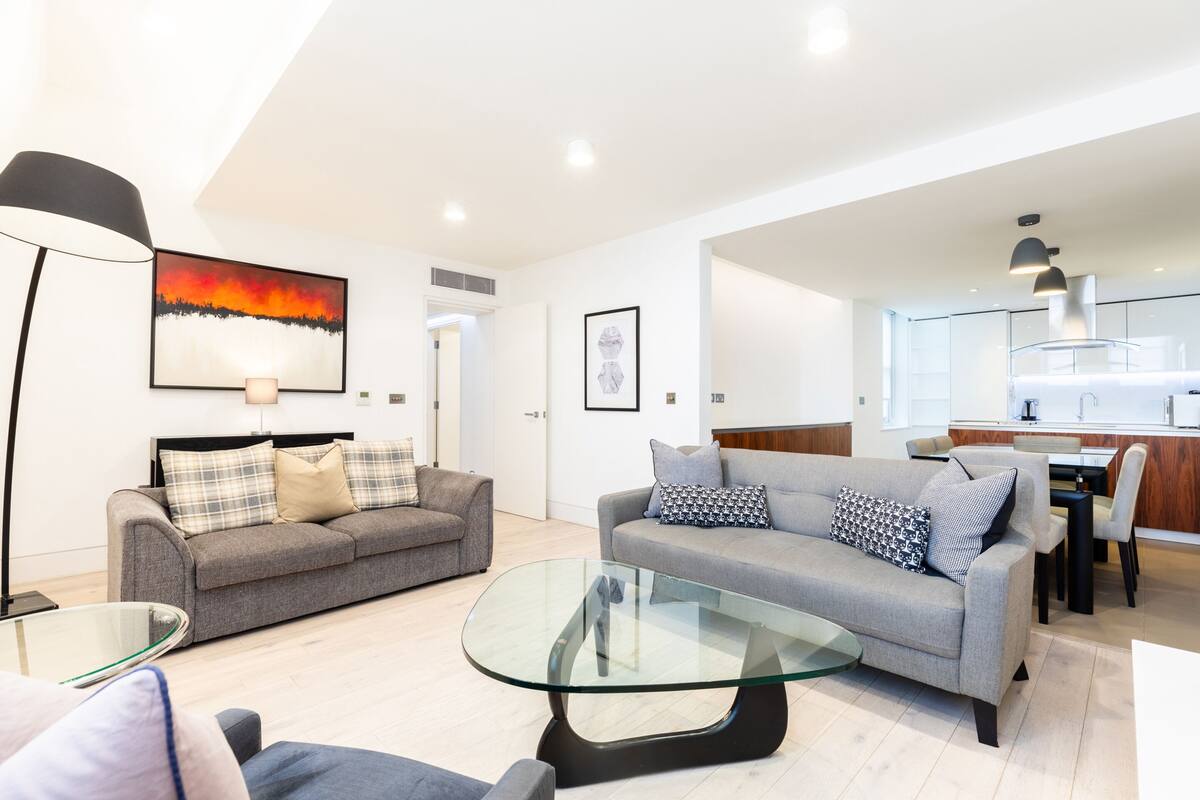 A modern living room with two sofas, a glass coffee table, and a dining area with a kitchen in the background.