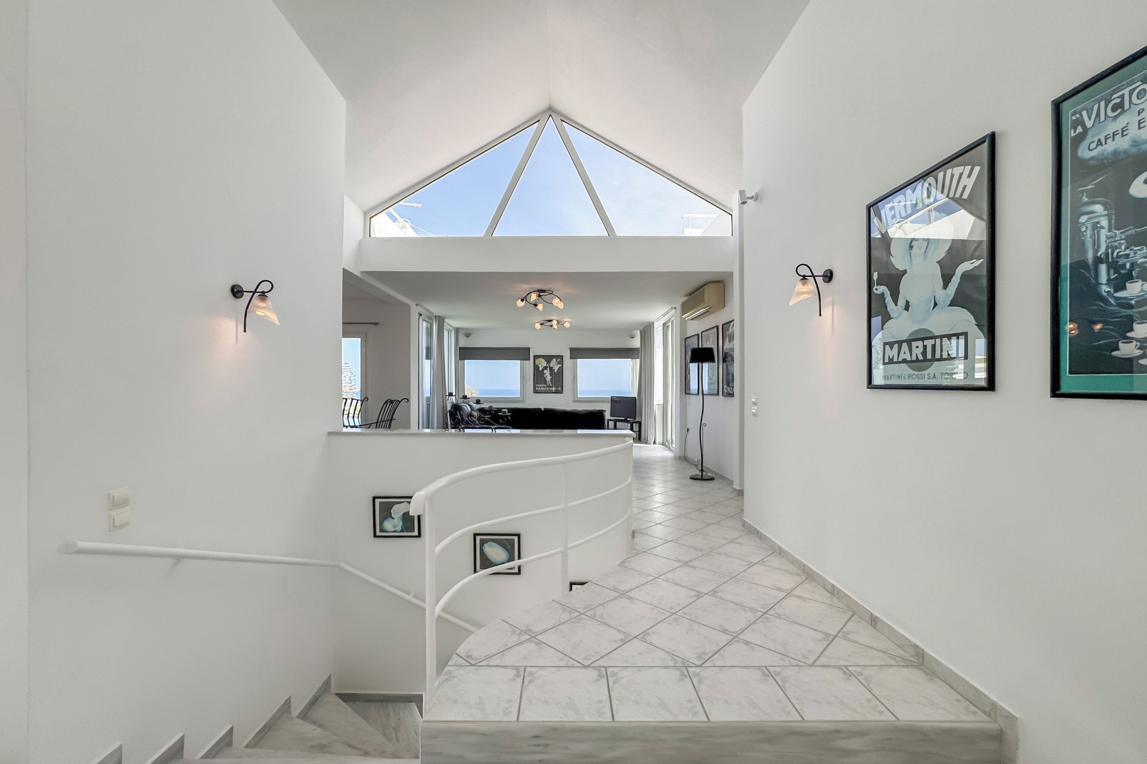 A spacious interior with a high ceiling, a central staircase, and a view to the outside.