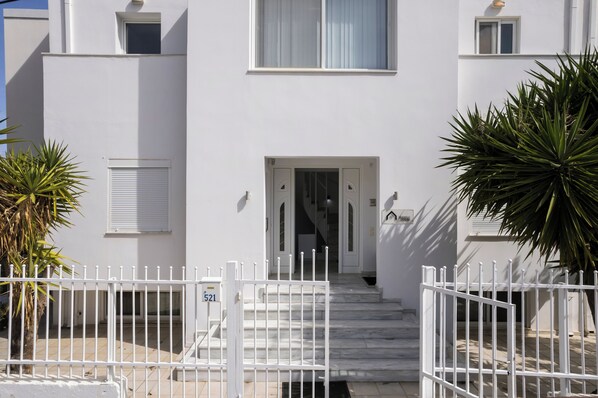 Un edificio bianco con una scala che conduce a una porta, una recinzione bianca e una palma.