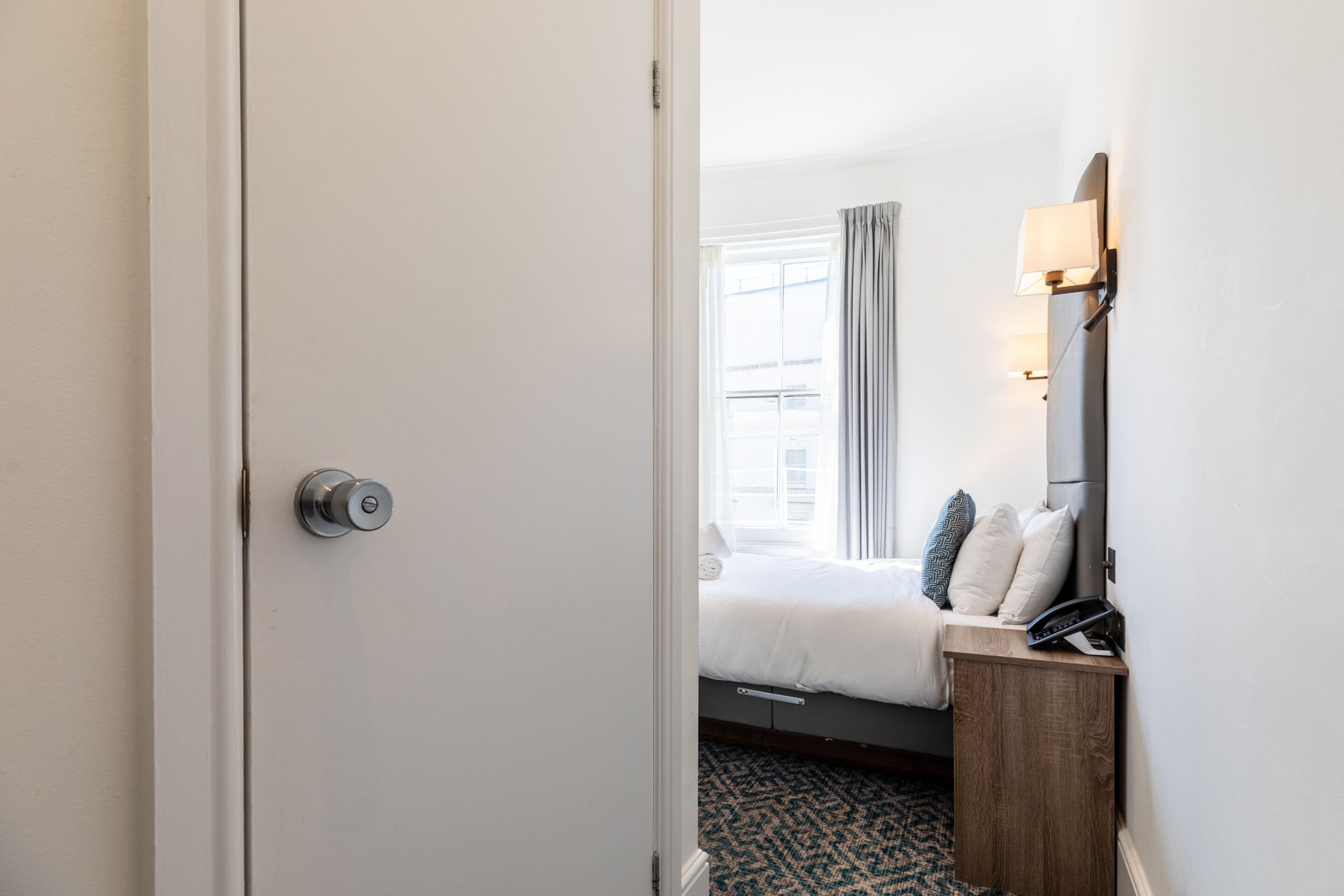 Une chambre d’hôtel avec un lit, une table de chevet avec une lampe et une fenêtre avec des rideaux.