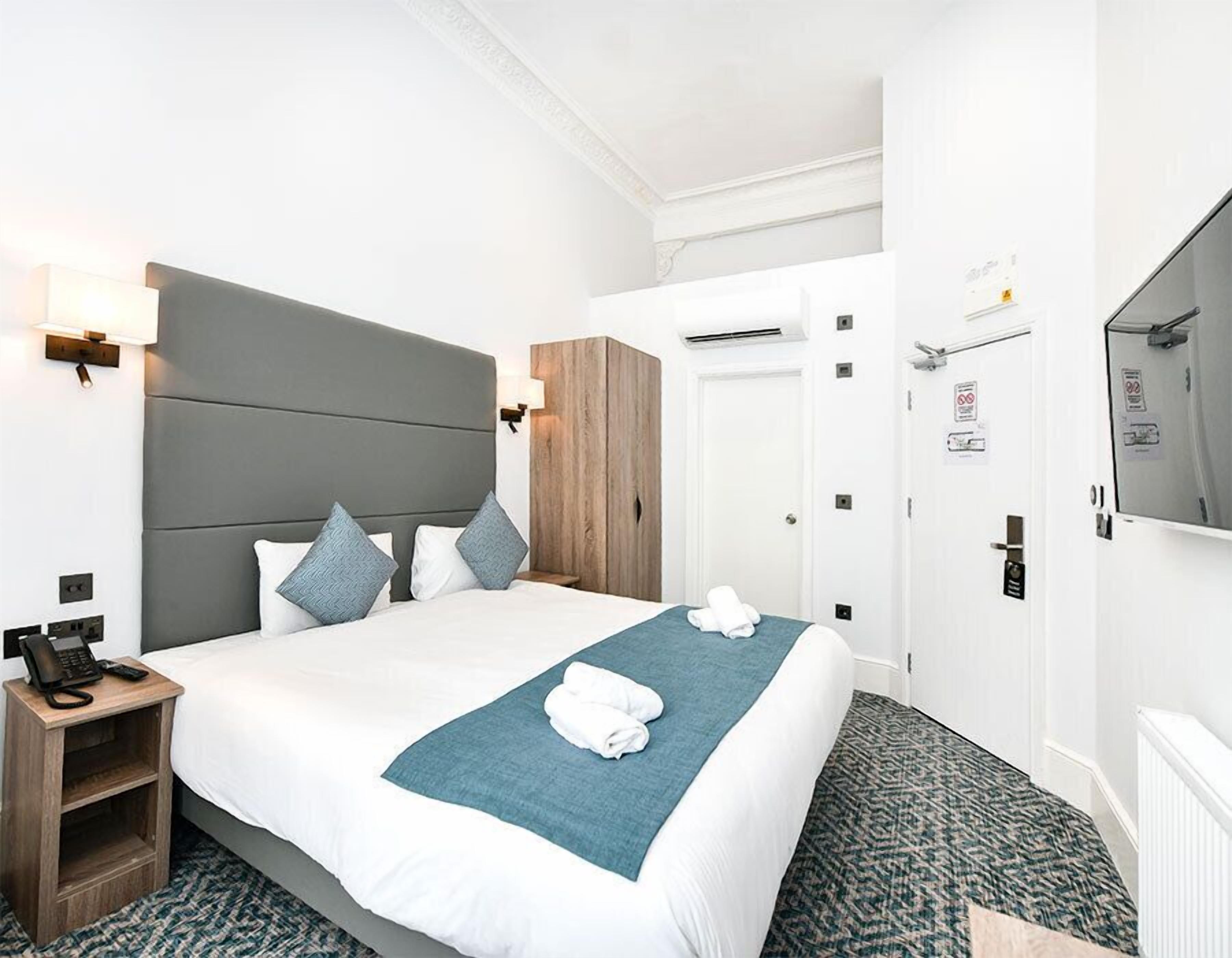 A hotel room with a bed, bedside table, wall-mounted TV, and a wardrobe.