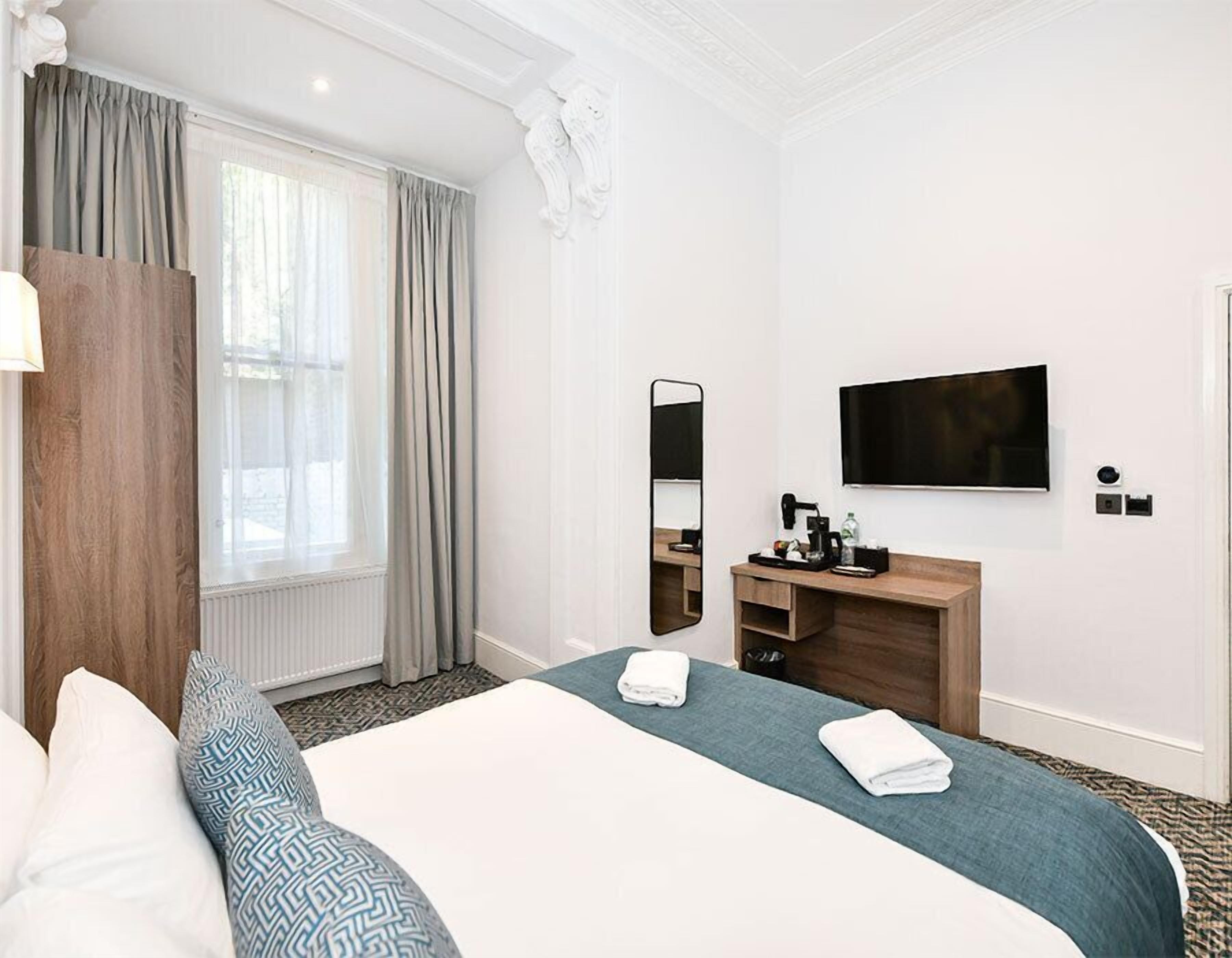 Ein Hotelzimmer mit Bett, Schreibtisch, Flachbildfernseher, Spiegel und einem fenster mit Vorhängen.