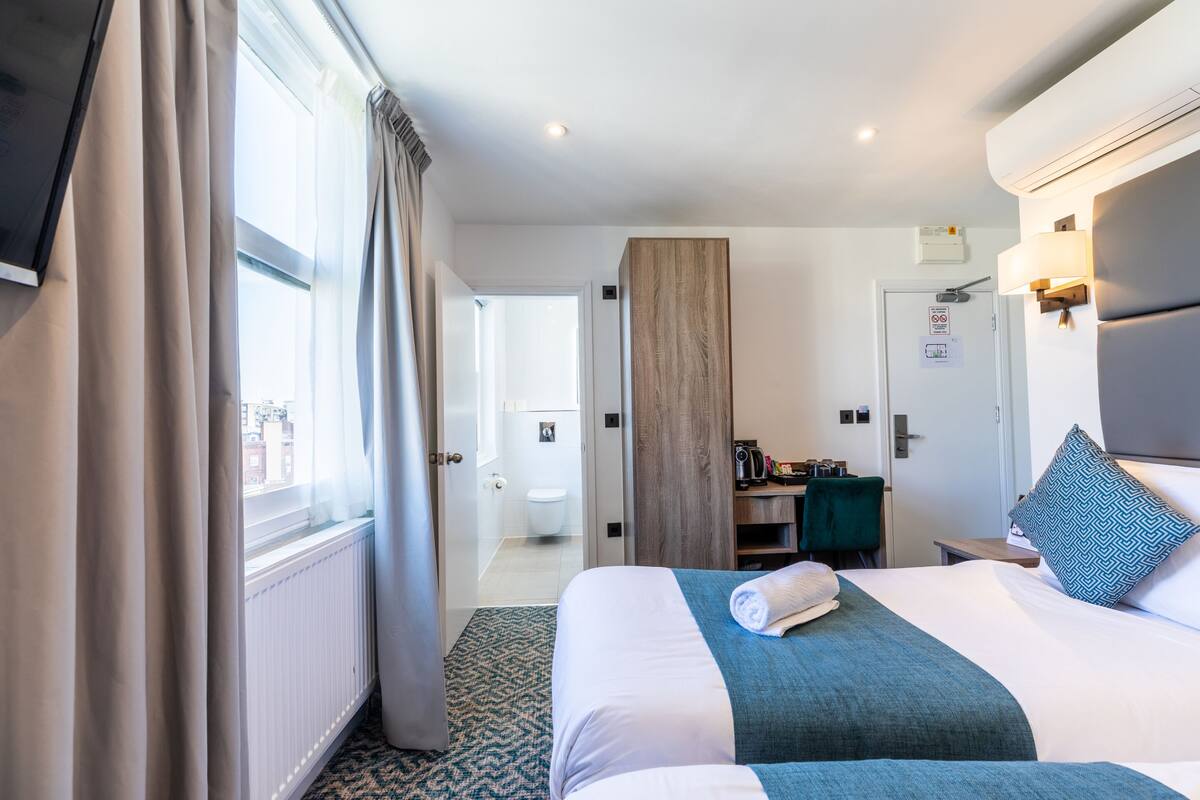 A hotel room with a large bed, a desk, a chair, a wardrobe, and a bathroom visible through an open door.