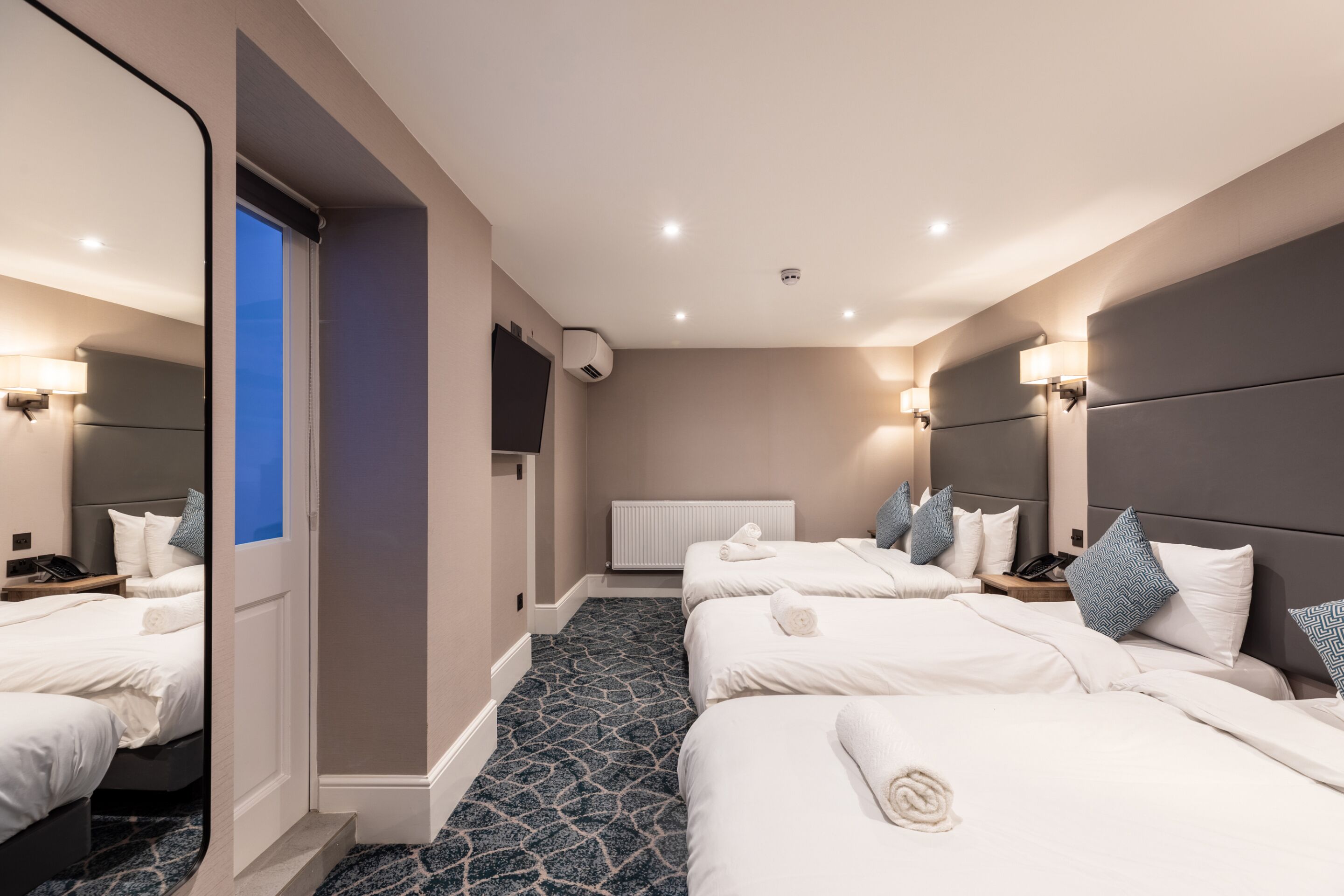 A hotel room with three beds, a large mirror, and a blue patterned carpet.