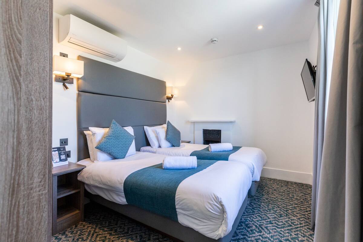 A hotel room with two beds, a bedside table with a phone, and a wall-mounted TV.